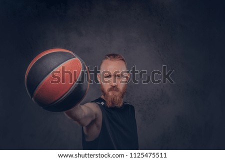 Portrait of a redhead basketball player in a black sportswear holding ball, isolated on dark textured background.