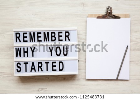 Noticeboard, pencil and 'Remember why you started' words on lightbox over white wooden background, from above. Top view, flat lay, overhead. 