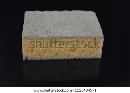On a black glossy background, a kitchen sponge is laid and lies, a washcloth for washing yellow and gray greens with reflection