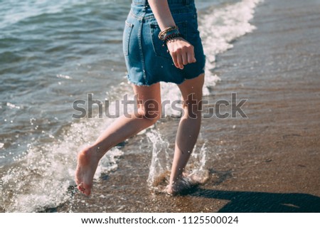 Young girl runs along the sea sandy beach barefoot, concept, legs