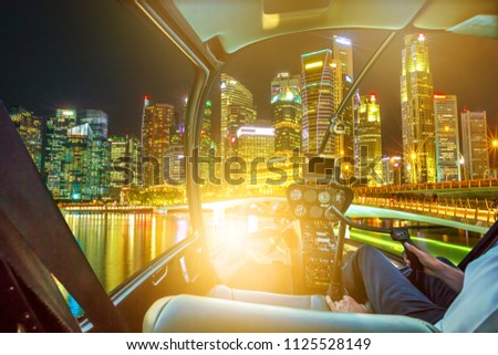 Helicopter cockpit on Singapore downtown skyline with skyscrapers of Business District and bridge in marina bay promenade. Scenic flight above Singapore with the lights of night reflects in the bay.