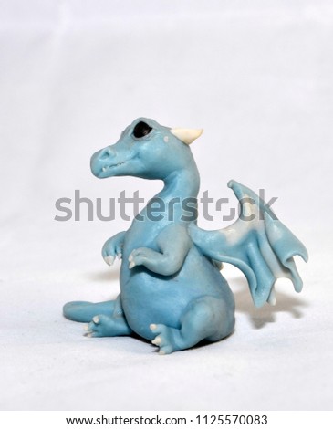 Blue baby-dragon sitting on a white surface, right side view