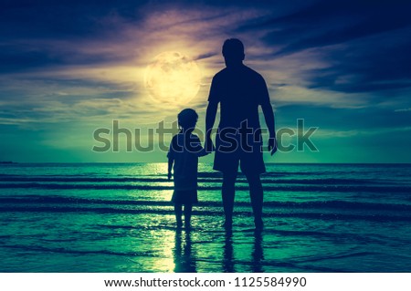 Silhouette back view of loving child holding hands her father, standing in the sea. Family enjoying and relaxing on beach with full moon on sky background. Cross process. The moon taken with my camera