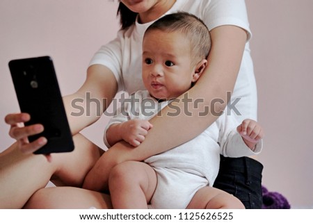 Mother with baby looking phone while sitting on the bed