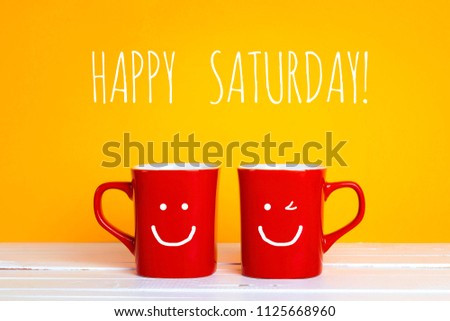 Two red coffee mugs with a smiling faces on a yellow background with phrase Happy saturday. Happy coffee mugs. Royalty-Free Stock Photo #1125668960