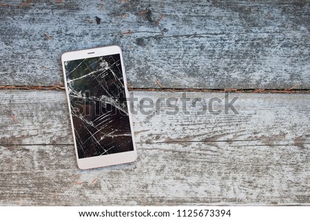 Mobile phone with broken screen on wooden background. Top view, copy space, fllat lay style.