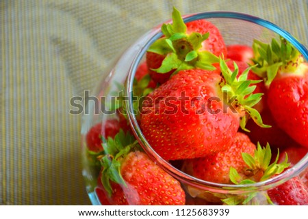 Red ripe strawberry with green leaves in a transparent glass vase in the shape of a ball on a beige background