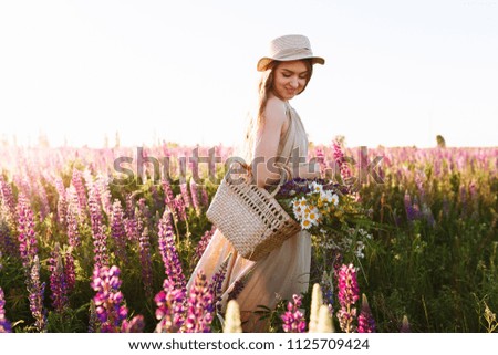 beautiful young woman in white dress and straw hat walking in flower field.