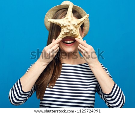 Smiling woman wearing hat holding starfish in front of face. Summer vacation concept portrait.