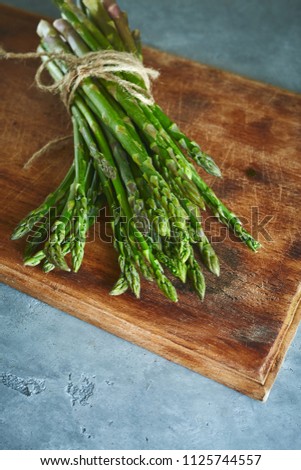 top view of bunch of fresh raw garden asparagus on rectangular wooden cutting board on gray concrete background. Ingredients for cooking. Food background.