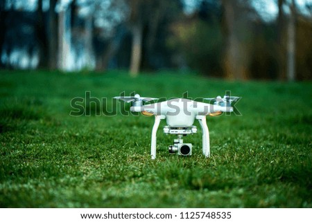 White quadrocopter, is ready for take off to fly high in the air, to take photos and record footage from above. Drone with four motors, propellers, camera and red warning lights on green background.