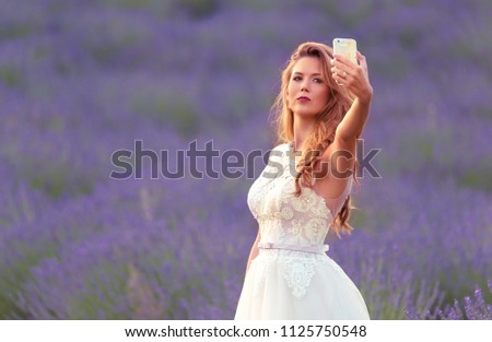 Happy bride take a selfie with her phone in lavender field. Beautiful blond woman