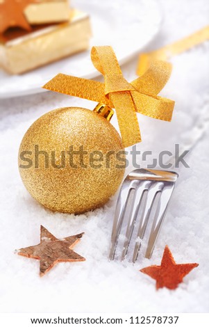 Golden Christmas Bauble with a bow and xmas stars and cutlery on snow background