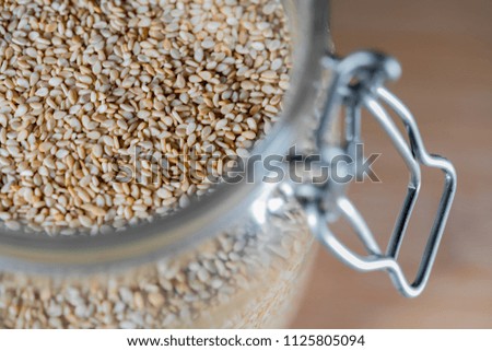Close up on some pale yellow sesame seeds in a glass mason jar. 
