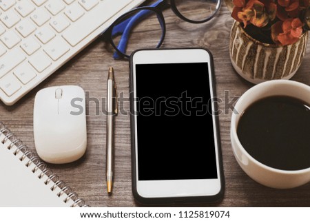 Selective focus top view with copy space and flat lay of the business office table with keyboard, mouse glasses, pen ,smartphone for mock up and coffee cup on wooden desk background