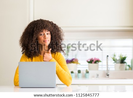 African american woman using computer laptop at kitchen happy with big smile doing ok sign, thumb up with fingers, excellent sign