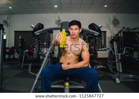 Asian man has muscle exercise in the gym.And Asian handsome muscles are tired, so drink Electrolyte drink.