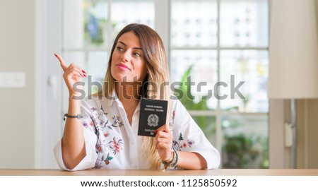 Young woman at home holding a passport of Italy very happy pointing with hand and finger to the side