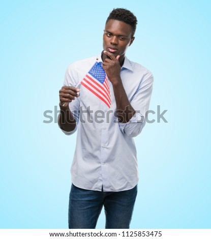 Young african american man holding USA flag serious face thinking about question, very confused idea