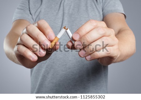 Close-up of male hands breaking a cigarette in half on grey background Royalty-Free Stock Photo #1125855302