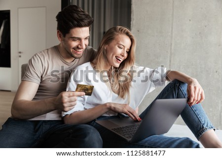 Photo of young happy loving couple in home indoors on sofa using laptop computer holding credit card.