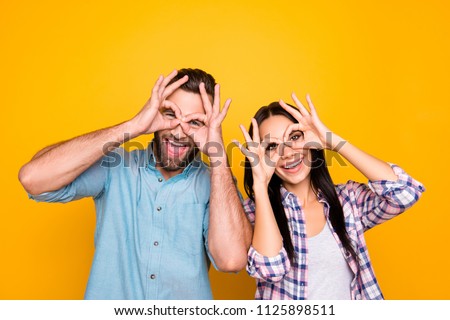 Joke humor ha-ha concept. Portrait of funky cheerful couple making binoculars with fingers wearing casual shirts isolated on bright yellow background