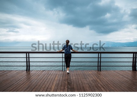 a girl stands in front of  fence on the lake 