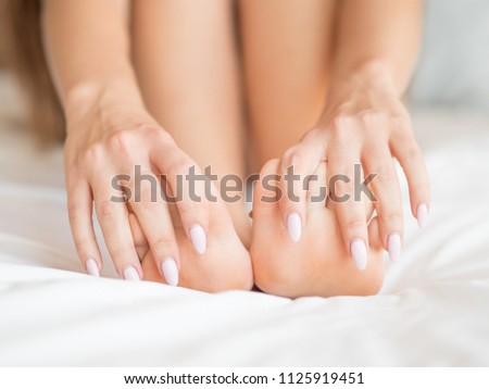 Female feet on a bed sheets. Close up photo of a woman massaging her feet.