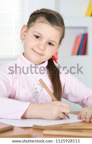Cute schoolgirl sitting at table and drawing 