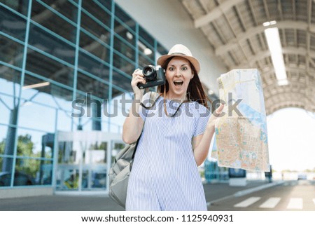 Young shocked traveler tourist woman in hat holding retro vintage photo camera, paper map at international airport. Female passenger traveling abroad to travel on weekends getaway. Air flight concept