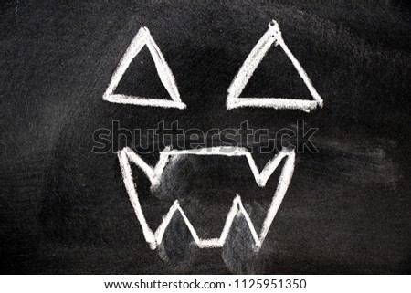 White color chalk hand drawing in ghost face shape on blackboard background