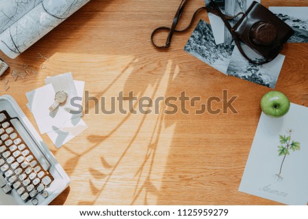 Stylish composition of wooden desk with croissant, map, floral poster, notebook and office accessories. Creative desk of traveler, poet, writer with copy space.