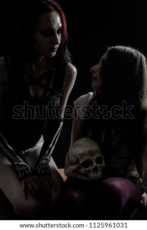 Two pretty gothic girls posing over dark background