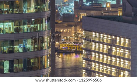 Windows of the multi-storey building of glass and steel lighting inside and moving people within timelapse. Aerial view of modern office skyscrapers in Dubai deira. Water of creek on background