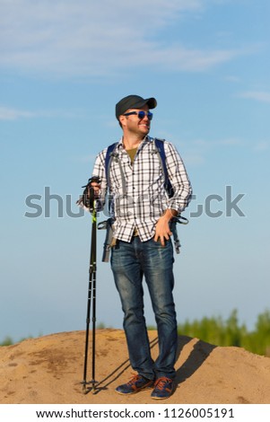 Photo of tourist man in sunglasses with sticks for walking on hill