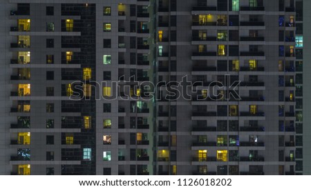 Windows of the multi-storey building of glass and steel lighting inside and moving people within timelapse. Aerial view of modern residential and office skyscrapers in Dubai marina. Pan down
