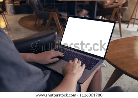 Mockup image of a woman using and typing on laptop with blank white desktop screen while sitting on a chair