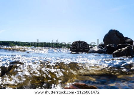 Big windy waves splashing over rocks. Wave splash in the lake against beach. Waves breaking on a stony beach, forming a spray. Water splashes. Water surface texture