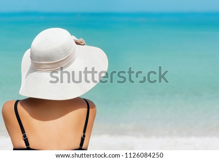 Happy woman enjoying beach relaxing joyful in summer by tropical blue water. Beautiful bikini model happy on travel wearing beach sun hat on beach. Girl on a tropical beach with hat