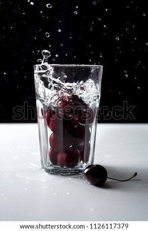 Cherry in the water. Glass filled with water and cherries. Red berry dropped into the water.  Splashes and drops on a black background. Glass of water with cherry