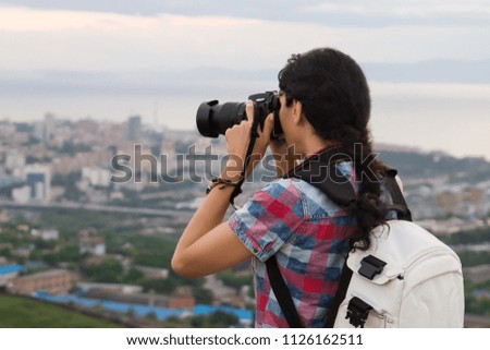 Woman photographer taking pictures of the city landscape from the view point on a summer day. Tourist takes a photo of the city. Travel concept. Girl with backpack and camera.