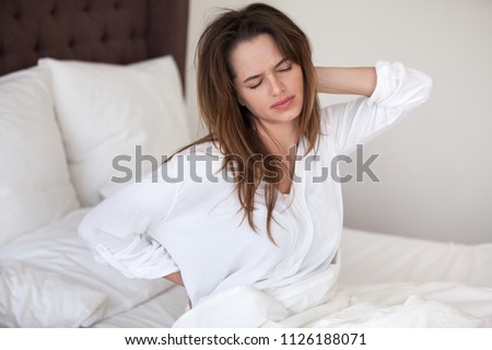 Unhappy young woman waking up in uncomfortable bed feeling ache in back pain massaging tensed muscles of stiff neck after sleep on bad mattress in incorrect posture, fibromyalgia and backache concept Royalty-Free Stock Photo #1126188071
