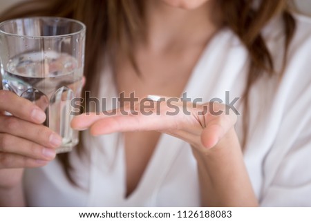 Woman holding pill and glass of water in hands taking emergency medicine, supplements or antibiotic antidepressant painkiller medication to relieve pain, meds side effects concept, close up view Royalty-Free Stock Photo #1126188083