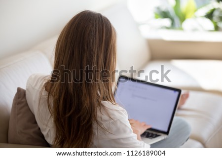 Woman using laptop for typing email at home, female blogger writer writing text for blog post, unemployed lady searching for work opportunities creating cover letter applying for new job, rear view Royalty-Free Stock Photo #1126189004