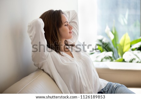 Relaxed calm woman resting breathing fresh air feeling mental balance enjoying wellbeing at home on sofa, satisfied young lady taking pleasure of stress free weekend morning stretching on couch