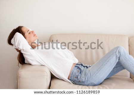 Calm happy millennial woman relaxing on couch breathing fresh air at home, lazy girl resting lying on comfortable sofa thinking positive enjoying peaceful good sunday weekend and stress free morning Royalty-Free Stock Photo #1126189859