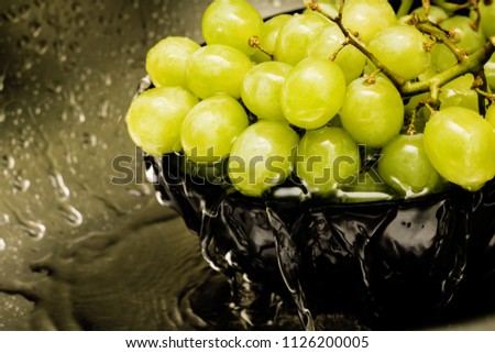 Green grapes in a black plate under running water, kitchen sink