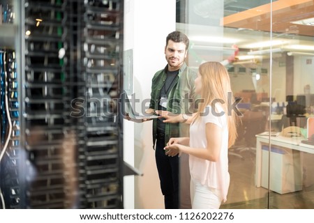 Two business people standing in server room with laptop and discussing Royalty-Free Stock Photo #1126202276