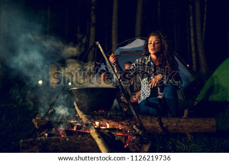 Shot of an attractive young woman cooking dinner while camping with her friends in the woods.