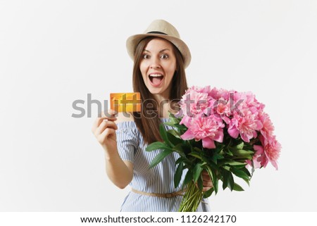 Young happy woman in blue dress, hat holding credit bank card, money, bouquet of beautiful pink peonies flowers isolated on white background. Business, delivery, online shopping concept. Copy space